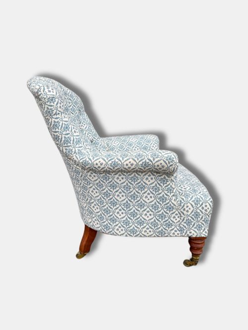 fig 1. A late Victorian button back armchair upholstered in blue and white botanical patterned fabric, featuring turned wooden front legs on brass castors.