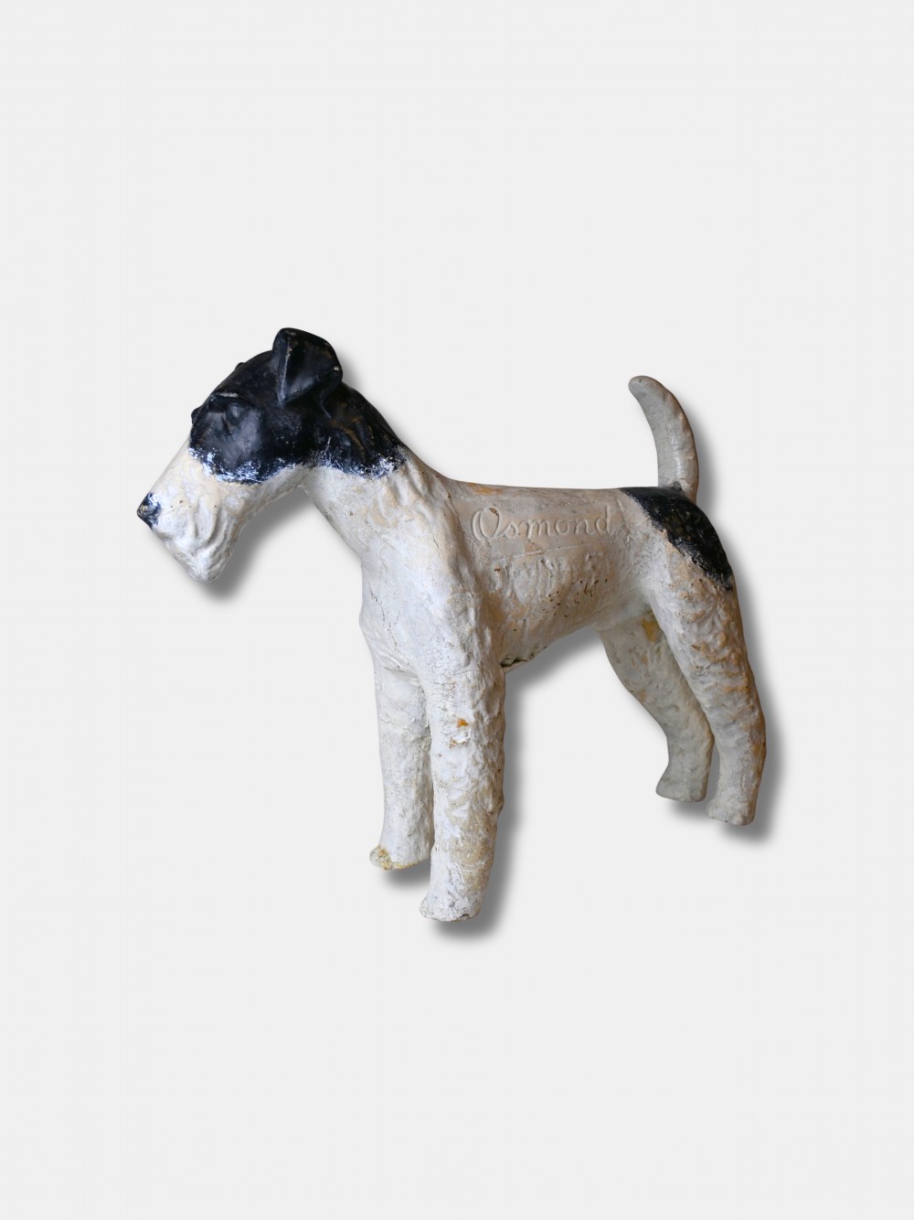 A life-size 1920s composition figure of a Fox Terrier featuring an off-white body, black painted markings on the head and back, and the name Osmond impressed into the shoulder.