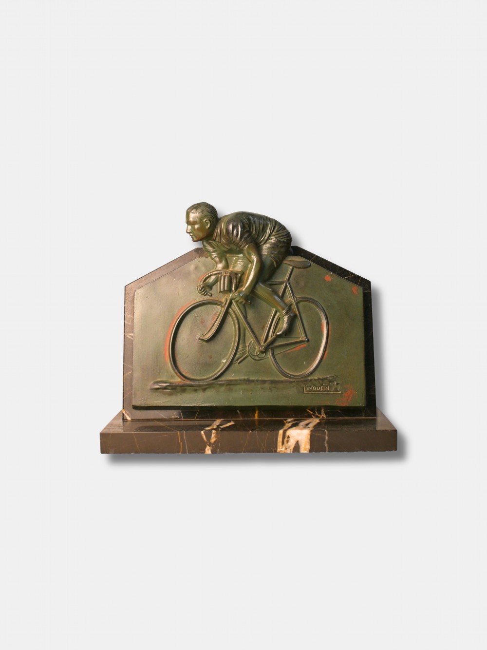 An Art Deco green patinated spelter relief sculpture depicting a cyclist leaning over handlebars, mounted on a veined black onyx plinth.