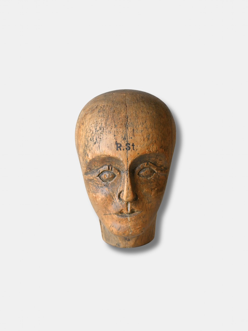 An antique carved wooden millinery head with rendered facial features and a stamped maker inscription on the forehead.
