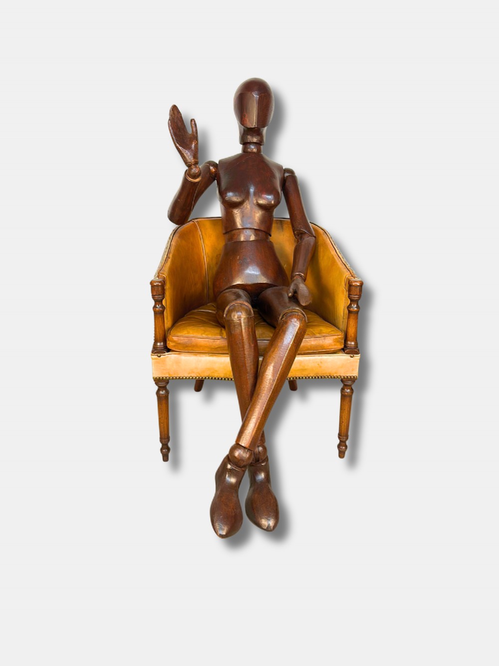 A life-size articulated female wooden lay figure depicted in a seated position with legs crossed and one hand raised.