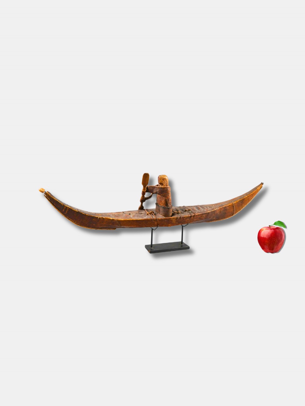 An 1882 Inuit model kayak crafted from tanned seal skin over a frame, featuring a central carved paddler figure holding a paddle, mounted on a modern black display stand.