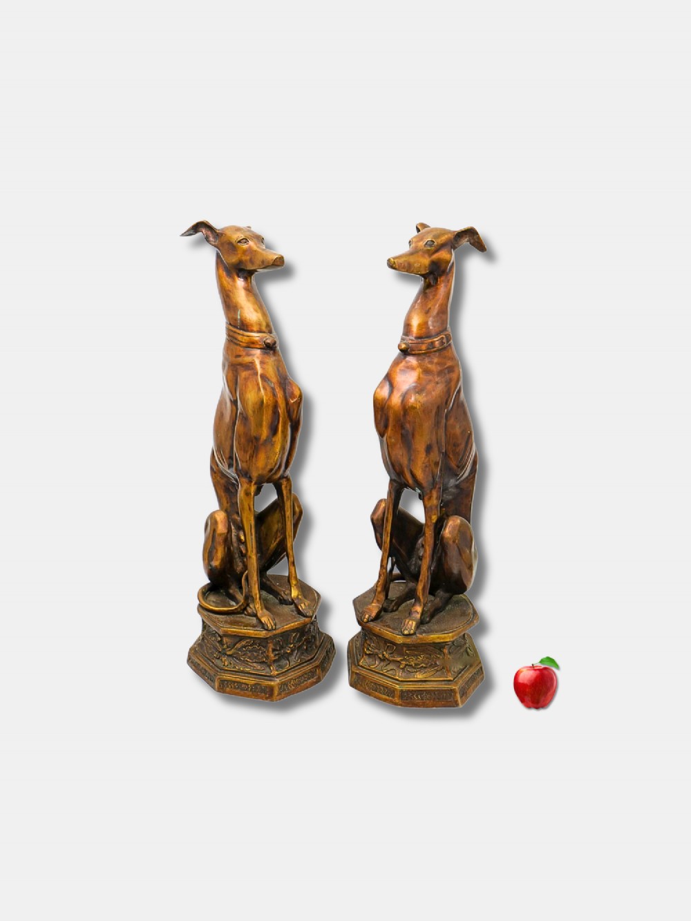 A pair of patinated bronze statues depicting upright seated greyhound dogs resting on relief-decorated octagonal pedestals.