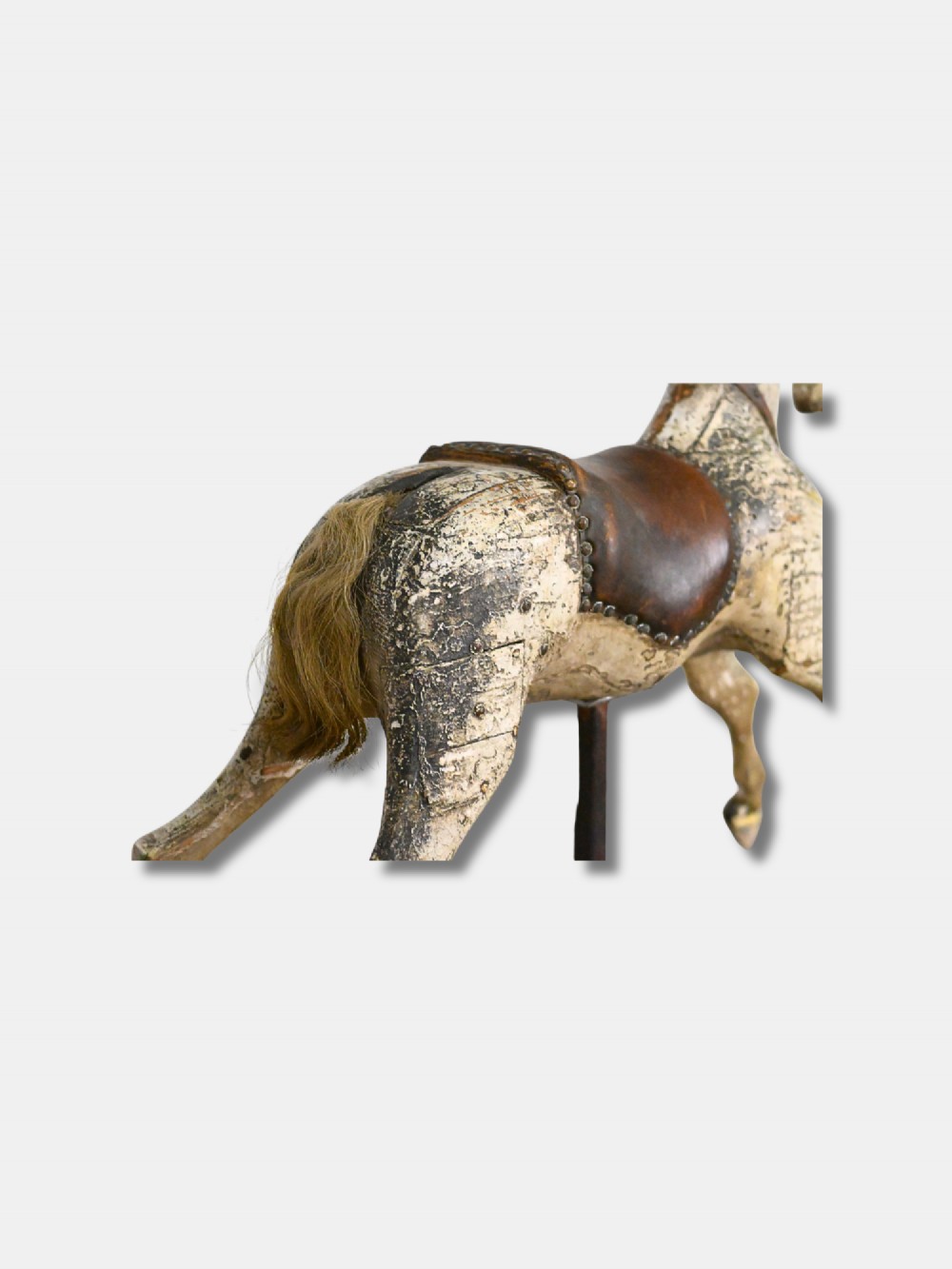 A carved 19th-century wooden rocking horse figure with distressed cream paint and a leather saddle, mounted on a dark metal display stand. View III