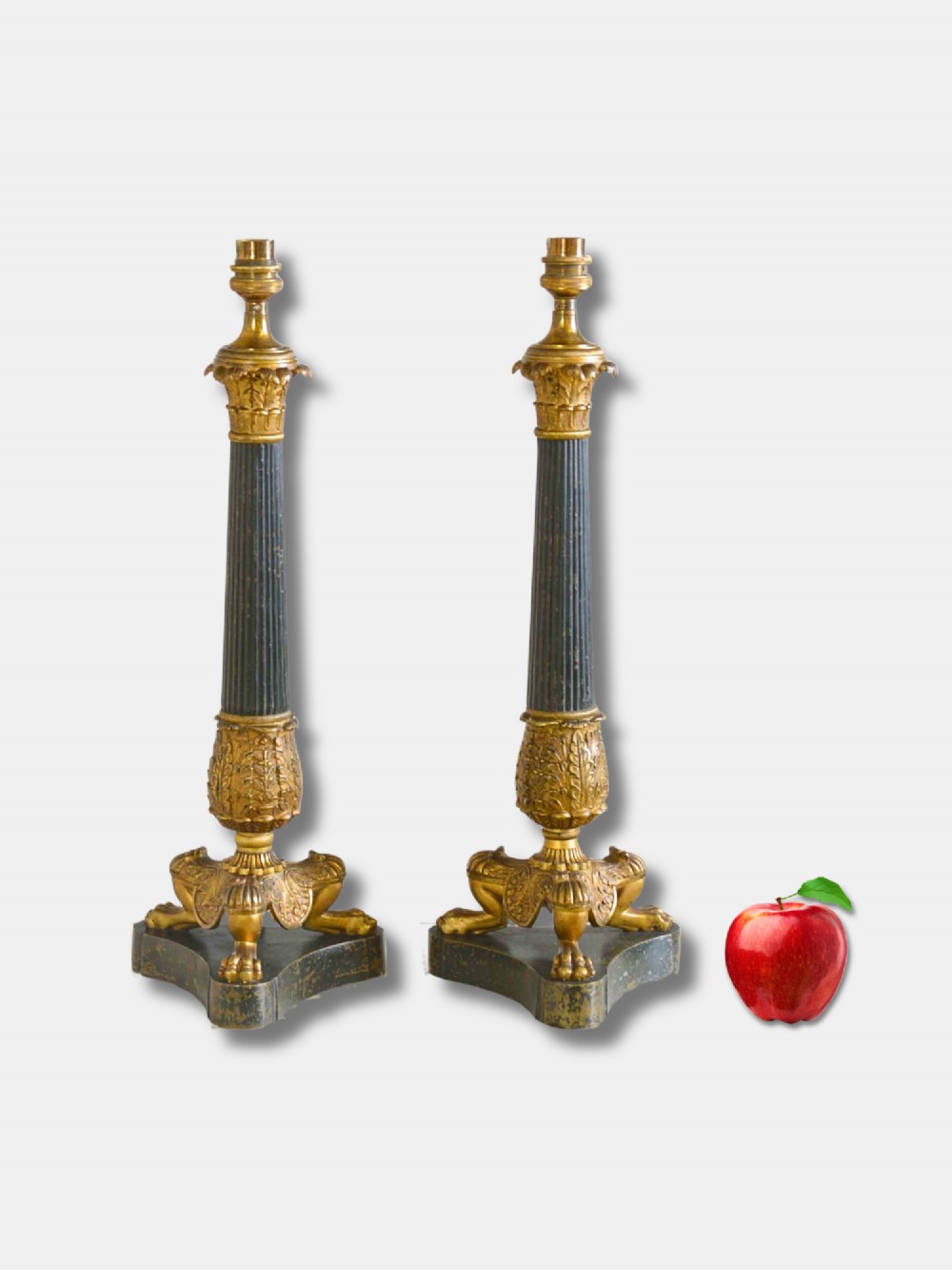 A pair of French Empire table lamps featuring dark fluted column shafts, gilded leaf capitals, lion paw feet, and triangular bases.