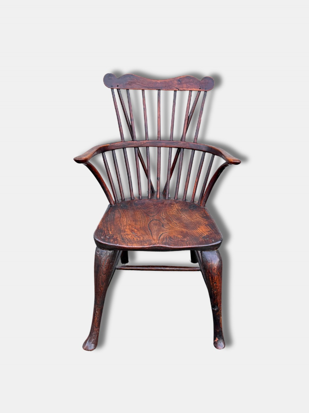 An antique dark wood comb-back Windsor armchair featuring turned back spindles, shaped top rail, curved arms, shaped wooden seat, and splayed legs.