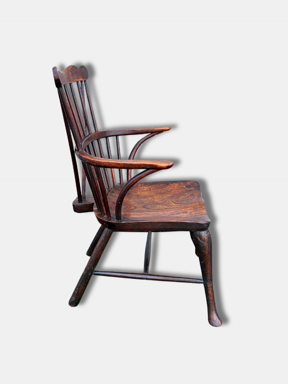 An antique dark wood comb-back Windsor armchair featuring turned back spindles, shaped top rail, curved arms, shaped wooden seat, and splayed legs. View II