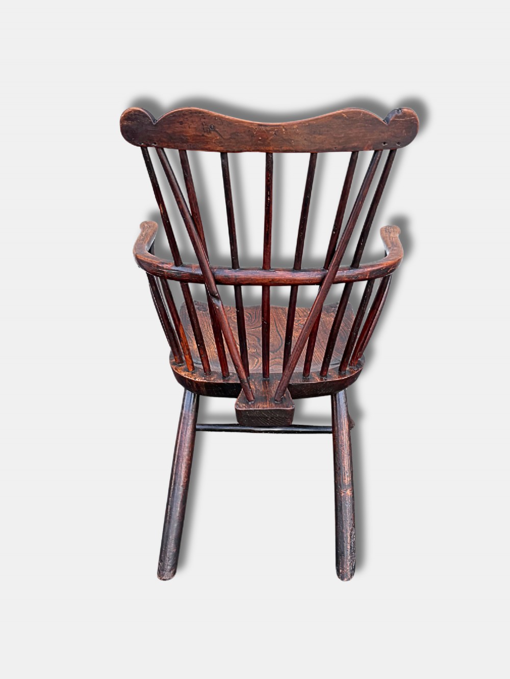 An antique dark wood comb-back Windsor armchair featuring turned back spindles, shaped top rail, curved arms, shaped wooden seat, and splayed legs. View III