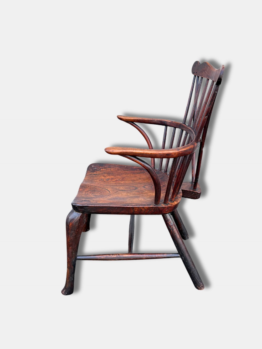 An antique dark wood comb-back Windsor armchair featuring turned back spindles, shaped top rail, curved arms, shaped wooden seat, and splayed legs. View IV