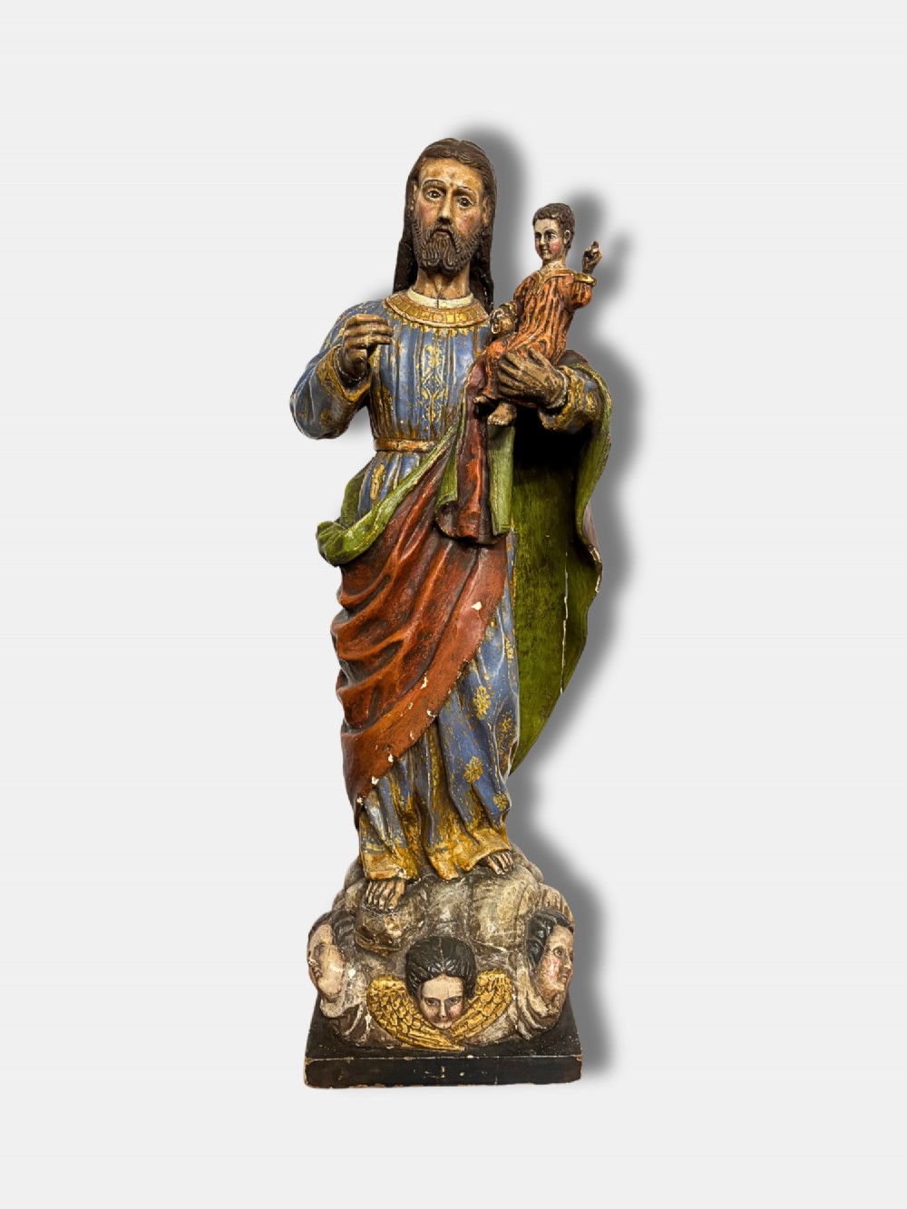 An 18th-century Peruvian carved polychrome wood statue of Saint Joseph holding the infant Jesus standing on a base decorated with cherub heads.
