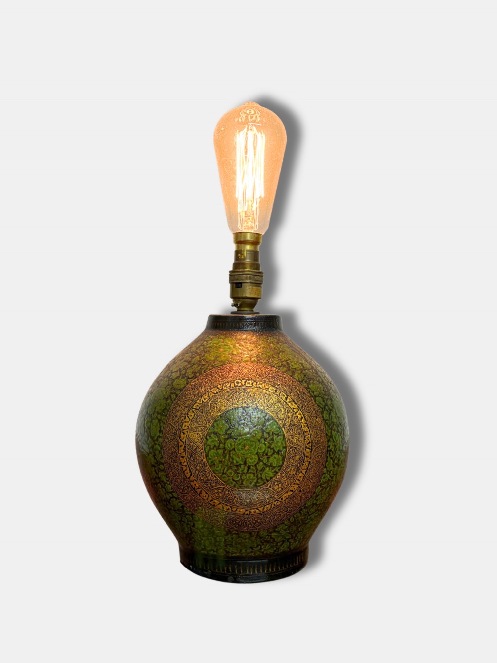 A rounded Kashmiri table lamp painted with intricate green and gilt floral patterns, topped with a brass light fitting and an exposed filament bulb.