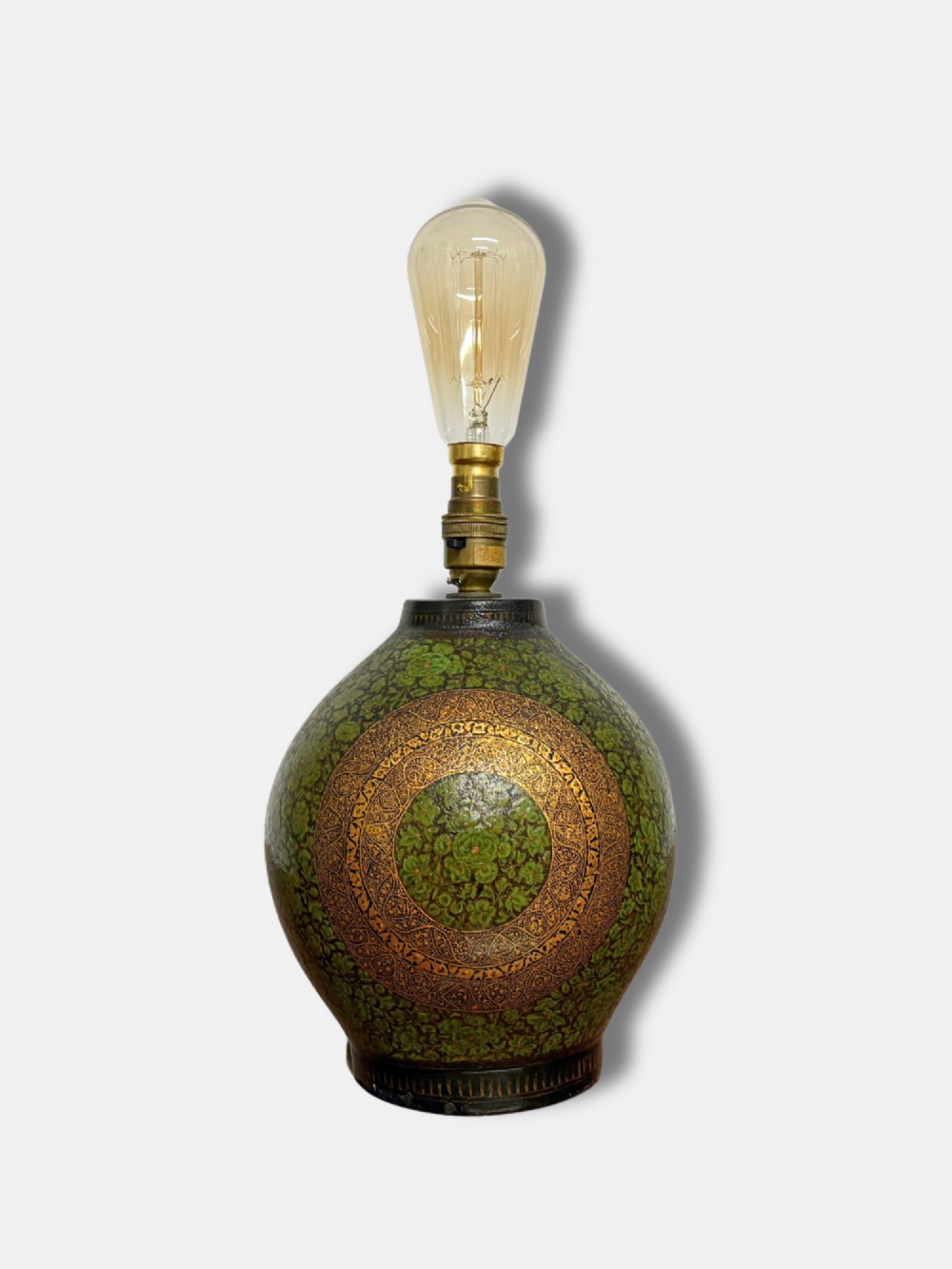 A rounded Kashmiri table lamp painted with intricate green and gilt floral patterns, topped with a brass light fitting and an exposed filament bulb. View II