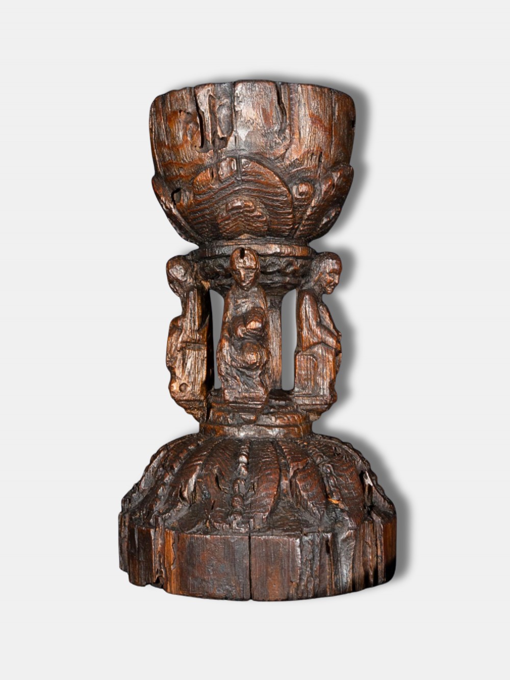 A 16th-century dark carved oak chalice featuring sculpted human figures around the stem and carved leaf motifs on the base and bowl.