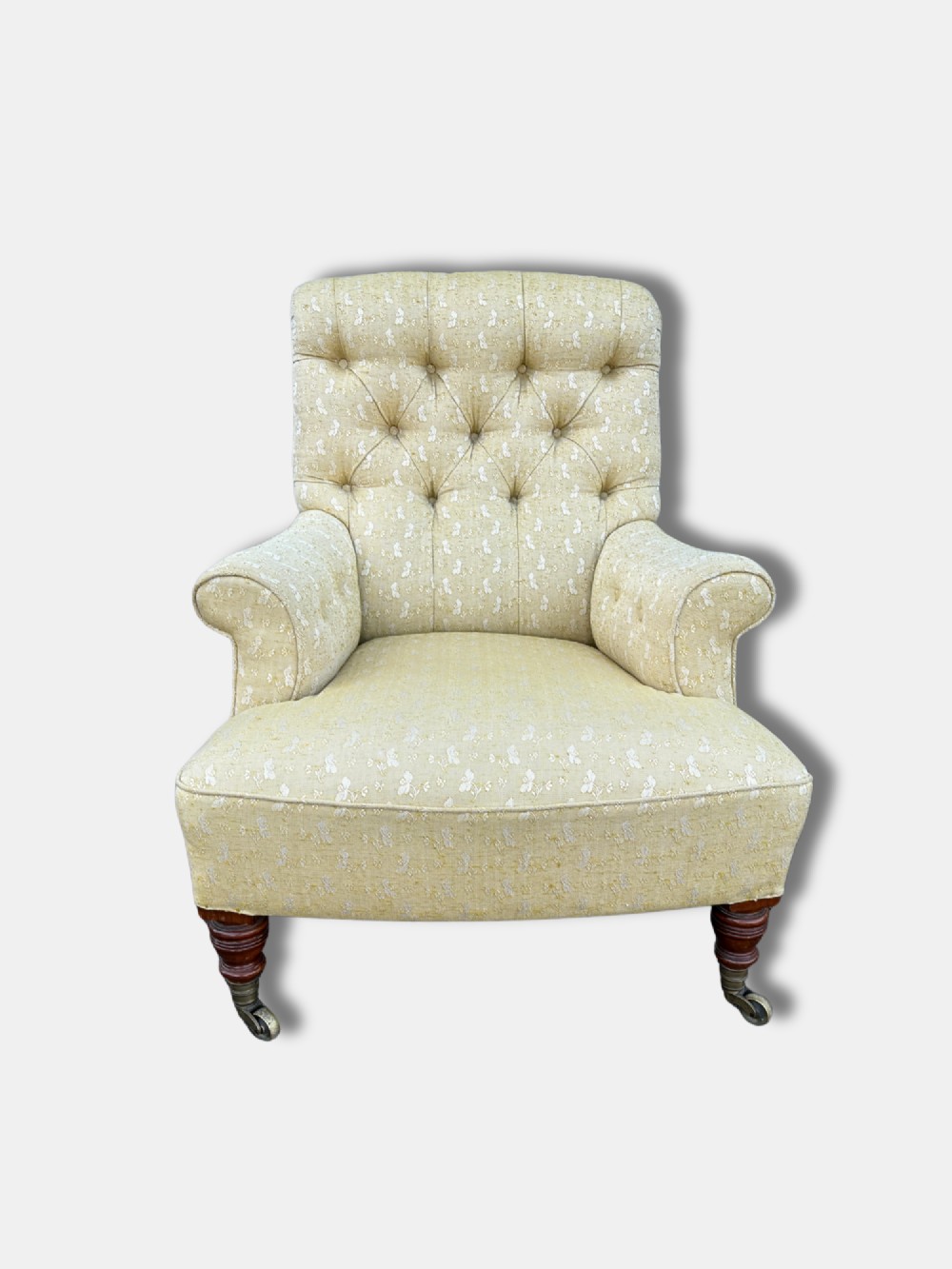 A Victorian armchair upholstered in pale yellow patterned fabric featuring a deep-buttoned backrest, scrolled armrests, and turned wood legs with brass castors. View II