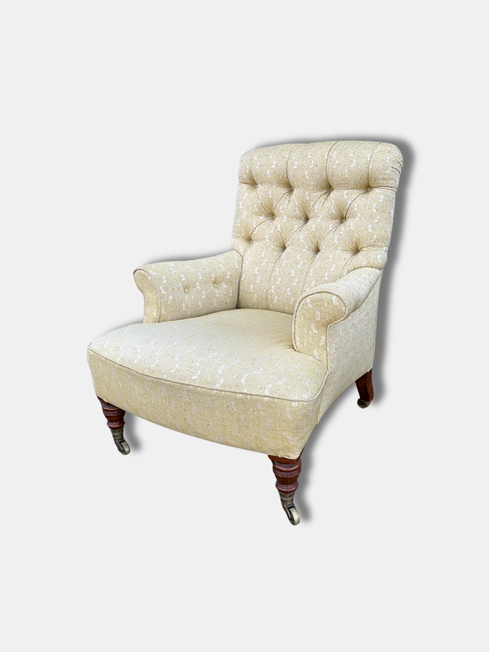 A Victorian armchair upholstered in pale yellow patterned fabric featuring a deep-buttoned backrest, scrolled armrests, and turned wood legs with brass castors. View III