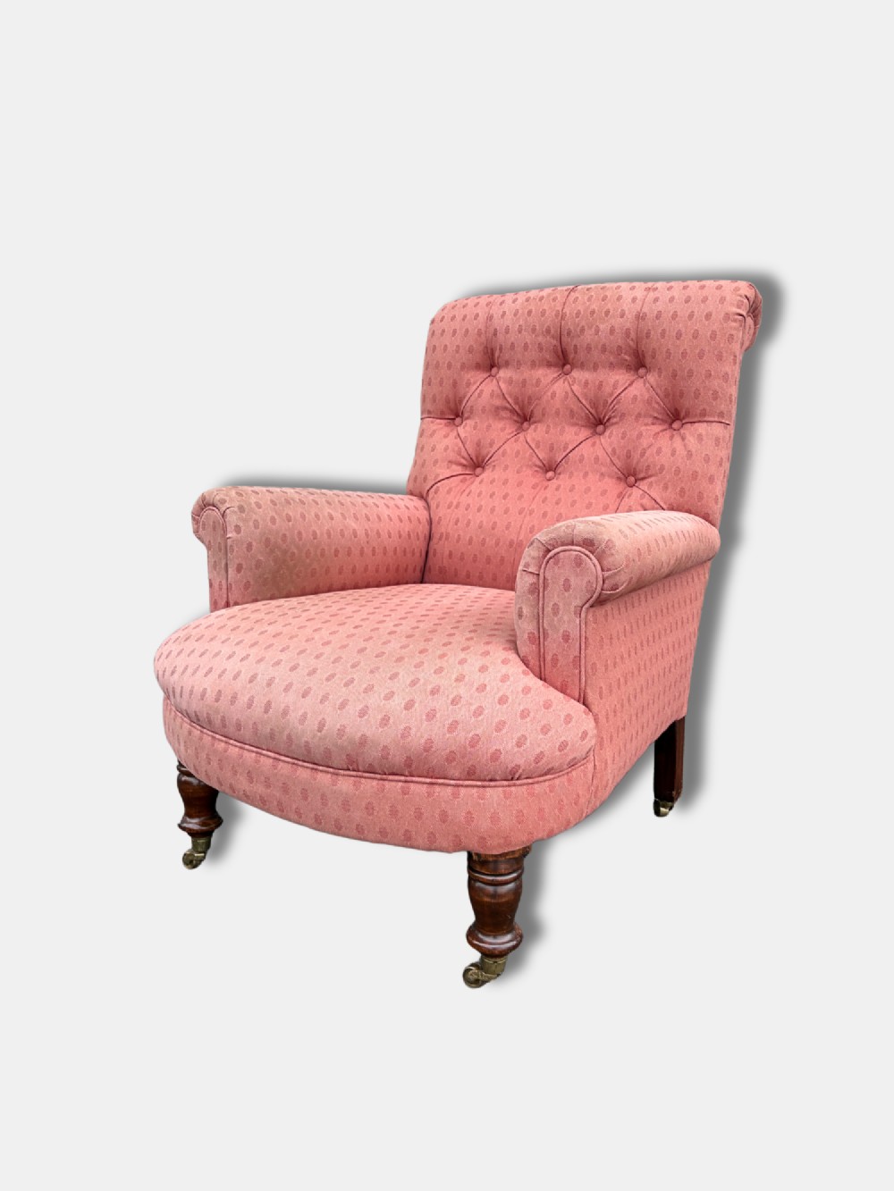 A late Victorian button-back armchair upholstered in dusty pink patterned fabric with low arms and turned wooden legs on brass castors. View III