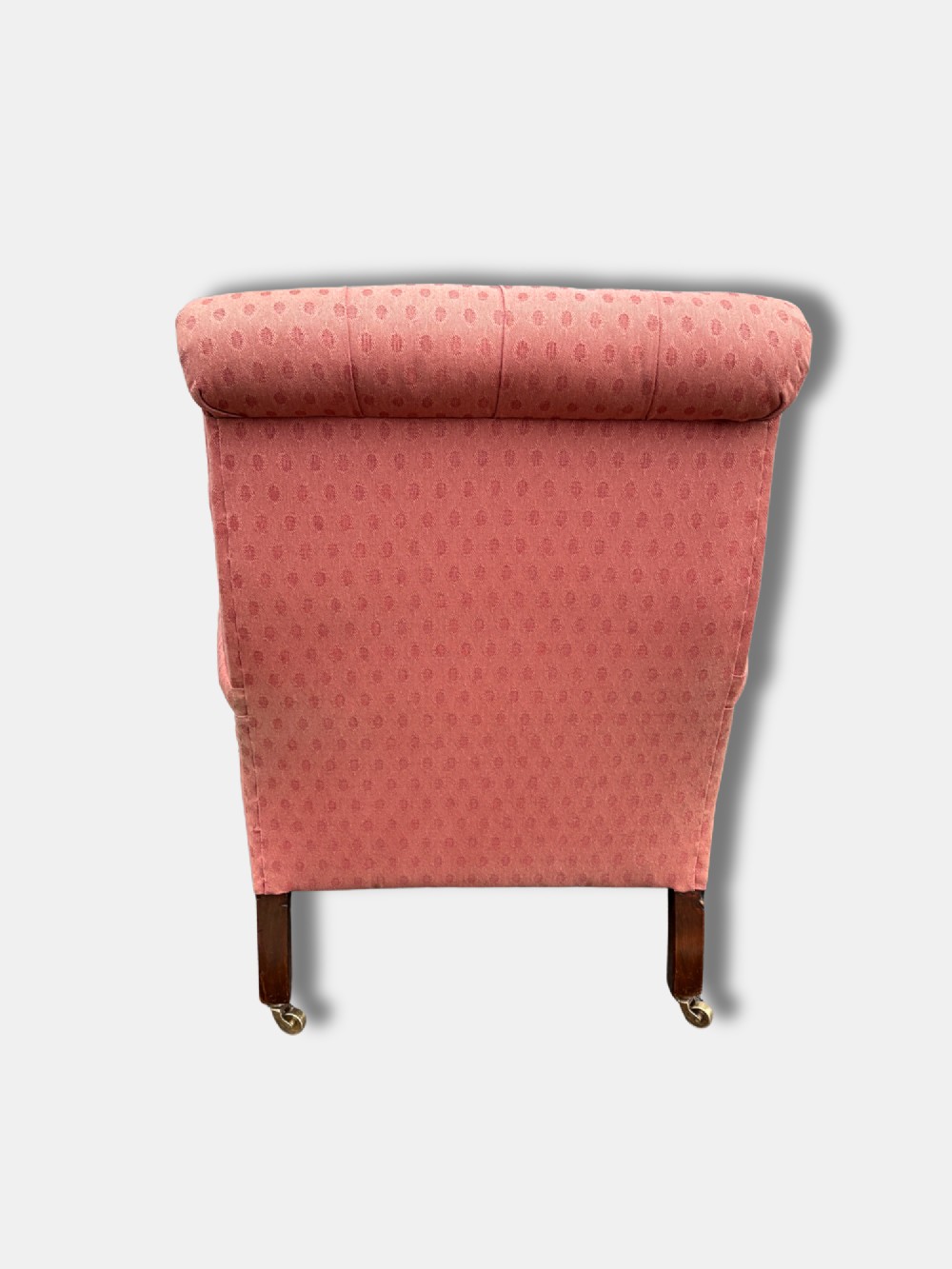 A late Victorian button-back armchair upholstered in dusty pink patterned fabric with low arms and turned wooden legs on brass castors. View IV