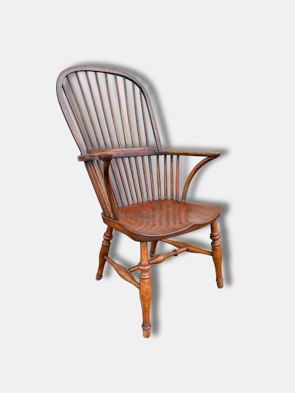 A nineteenth-century English stickback Windsor armchair made of ash and elm with turned legs, an H-stretcher, and a shaped saddle seat.