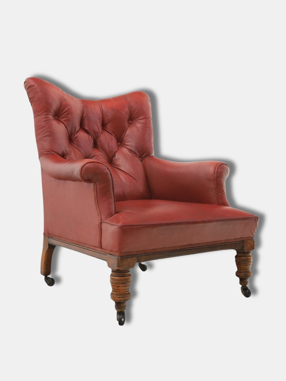 A pair of 1920s English armchairs upholstered in red oxblood rexine with deep buttoning and turned wooden legs on castors. View III