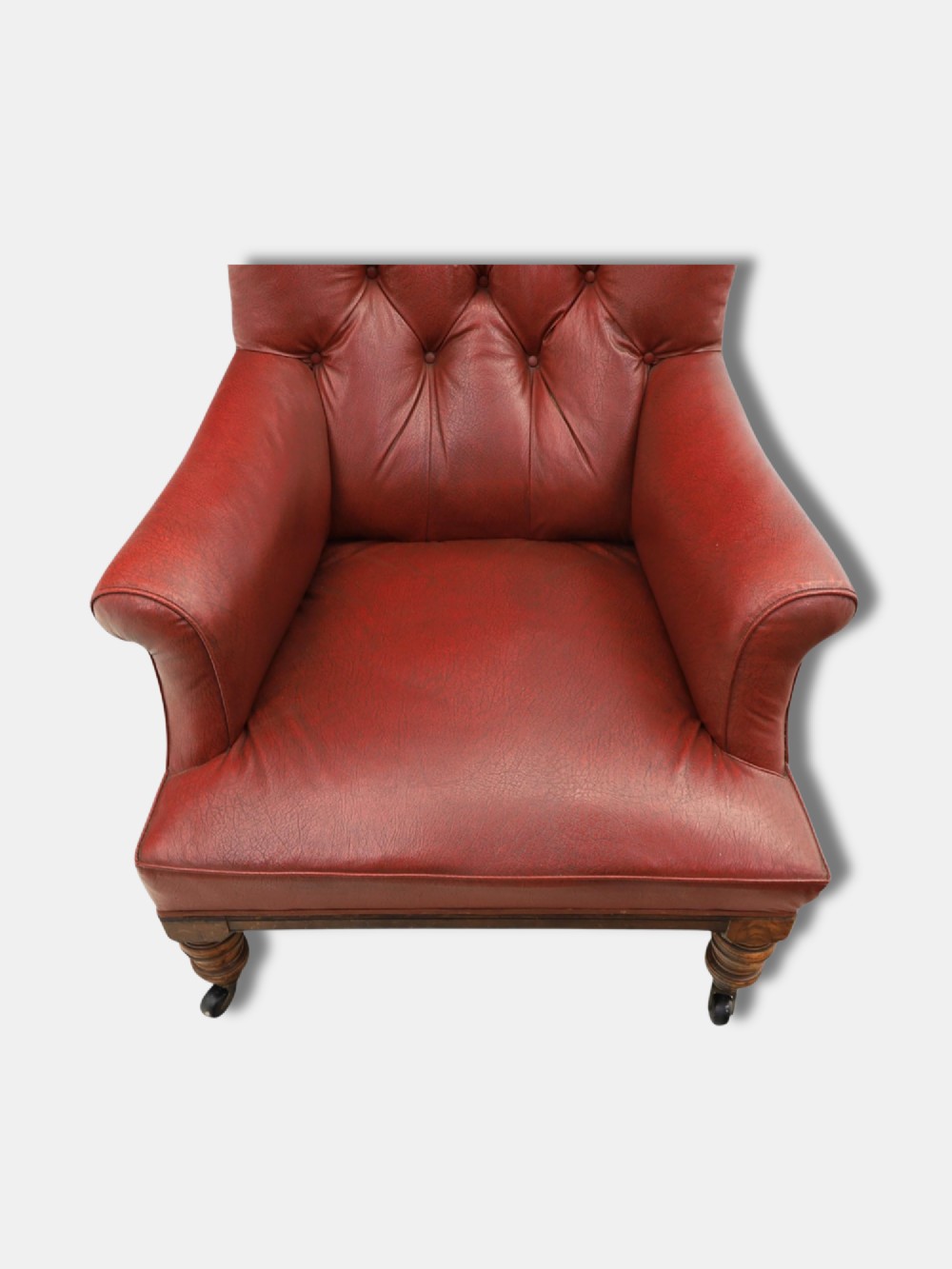 A pair of 1920s English armchairs upholstered in red oxblood rexine with deep buttoning and turned wooden legs on castors. View IV