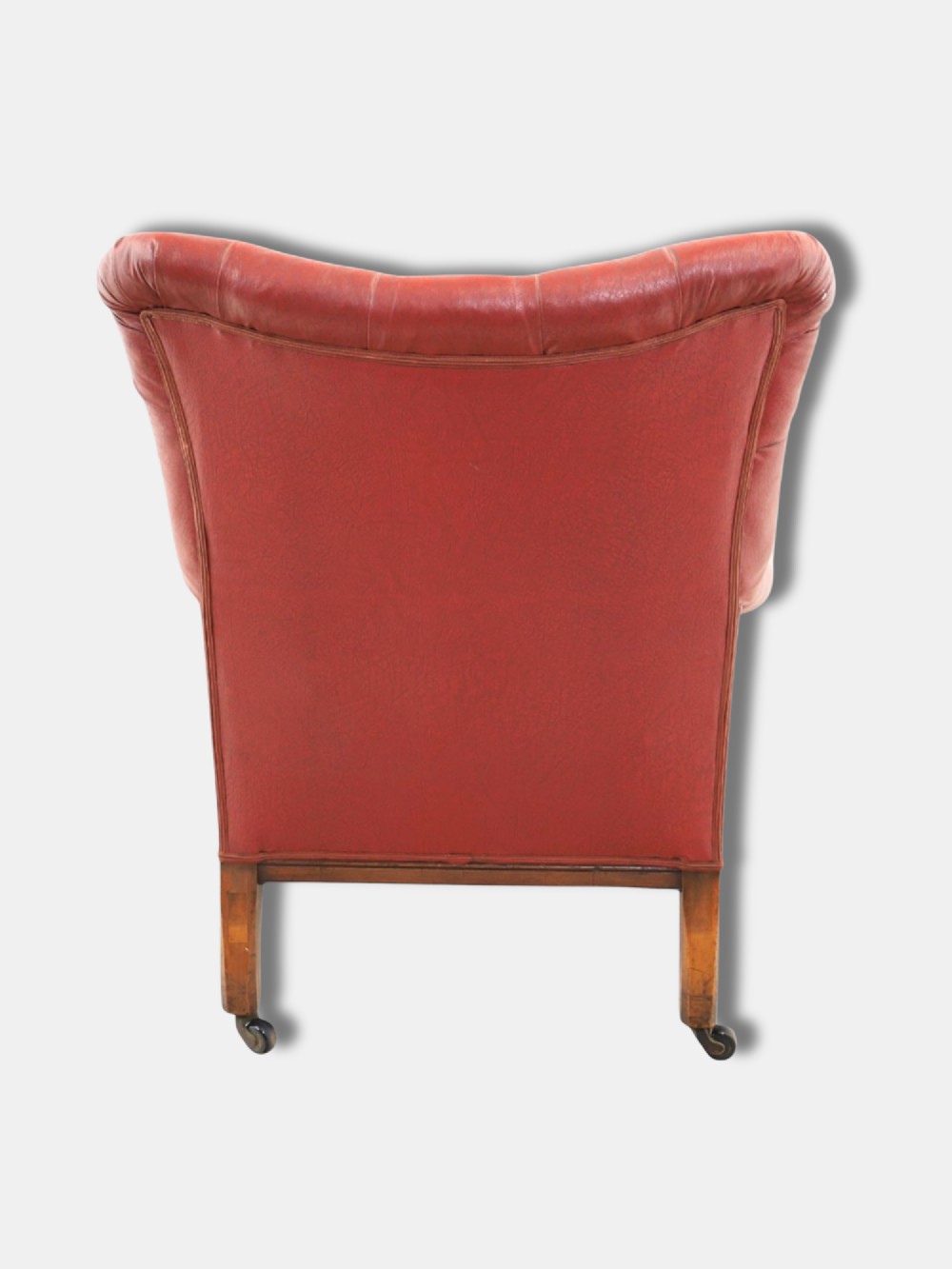 A pair of 1920s English armchairs upholstered in red oxblood rexine with deep buttoning and turned wooden legs on castors. View V