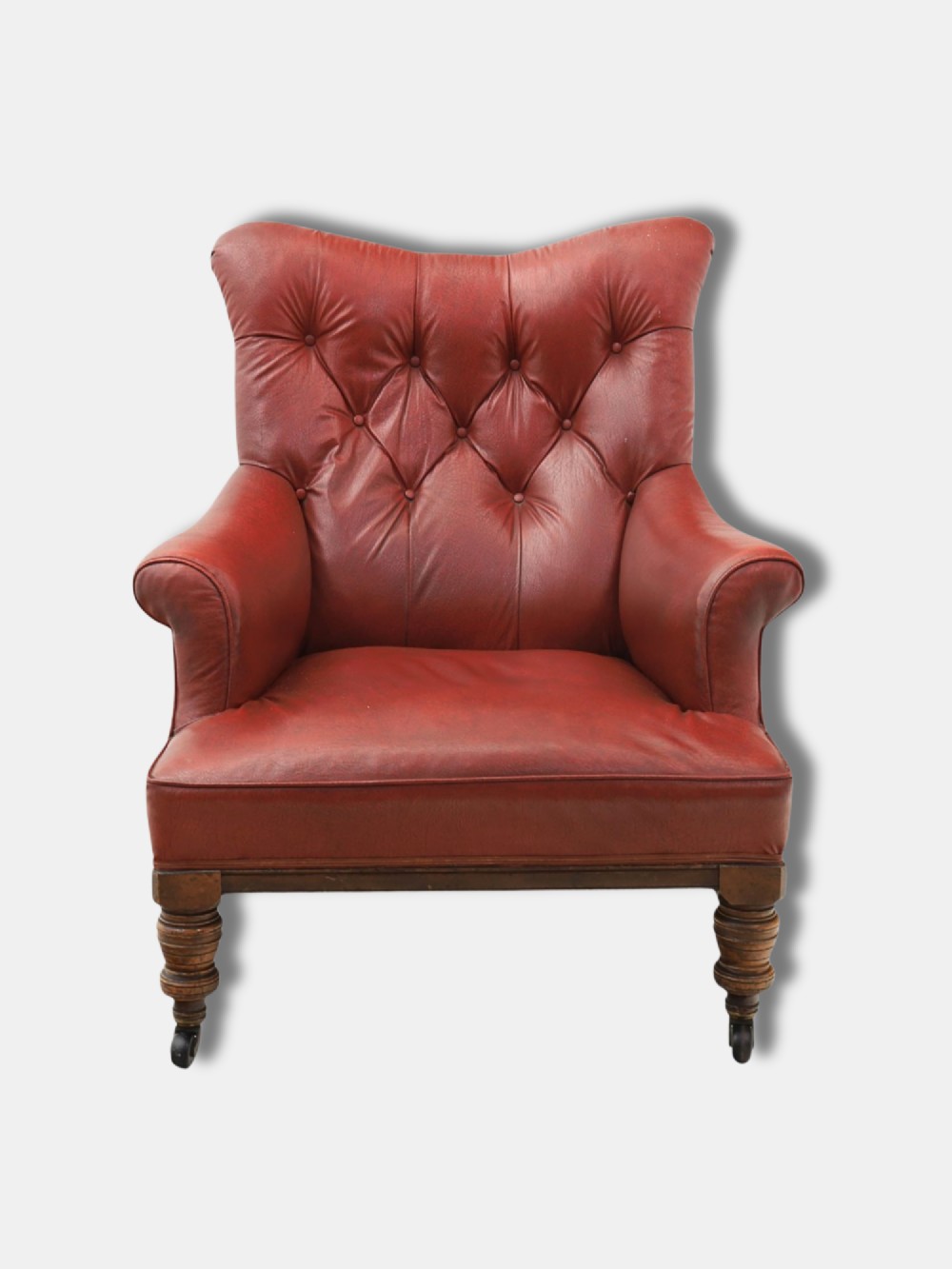A pair of 1920s English armchairs upholstered in red oxblood rexine with deep buttoning and turned wooden legs on castors. View VI
