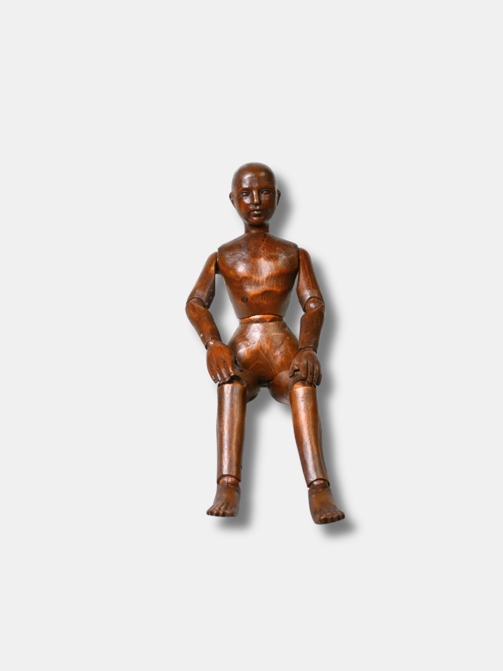 A French carved wood artist lay figure from circa 1890 with fully articulated limbs and a warm brown polished finish shown in a seated posture.