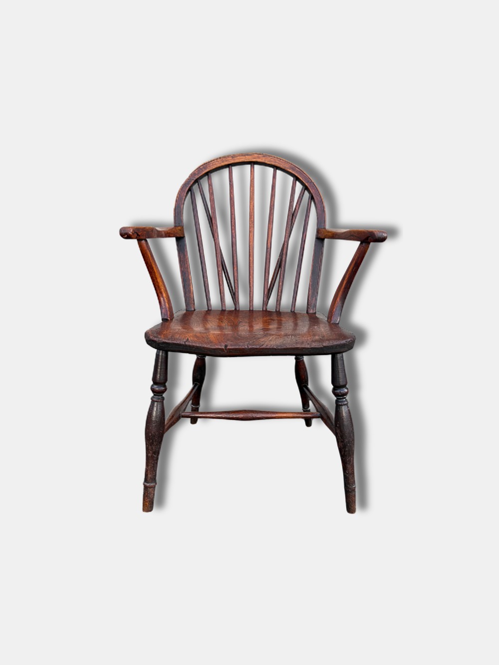 A dark brown antique Thames Valley Windsor armchair made of timber featuring a hoop back with spindles, curved armrests, a shaped solid seat, and turned legs.