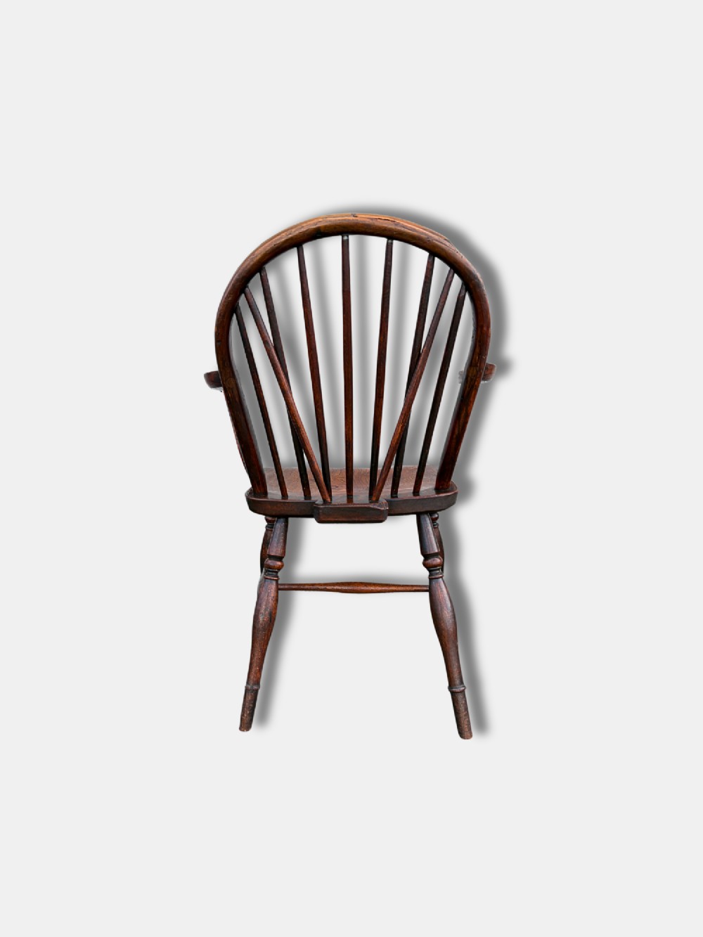 A dark brown antique Thames Valley Windsor armchair made of timber featuring a hoop back with spindles, curved armrests, a shaped solid seat, and turned legs. View III