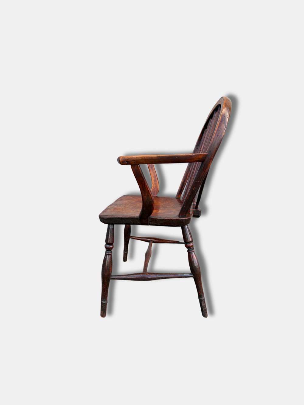 A dark brown antique Thames Valley Windsor armchair made of timber featuring a hoop back with spindles, curved armrests, a shaped solid seat, and turned legs. View IV