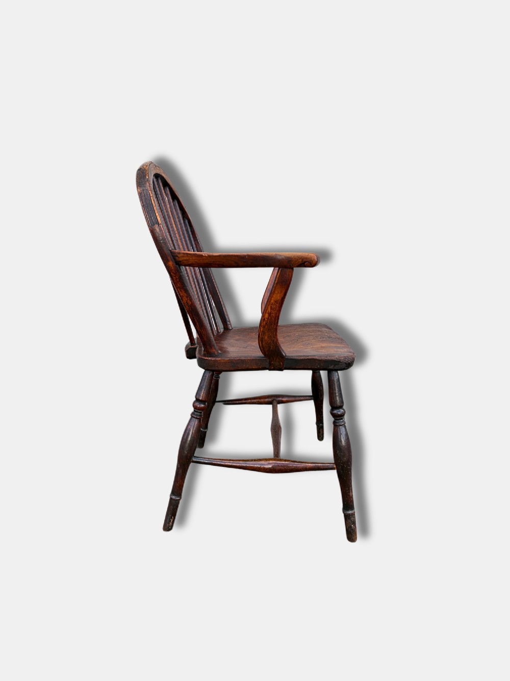 A dark brown antique Thames Valley Windsor armchair made of timber featuring a hoop back with spindles, curved armrests, a shaped solid seat, and turned legs. View V