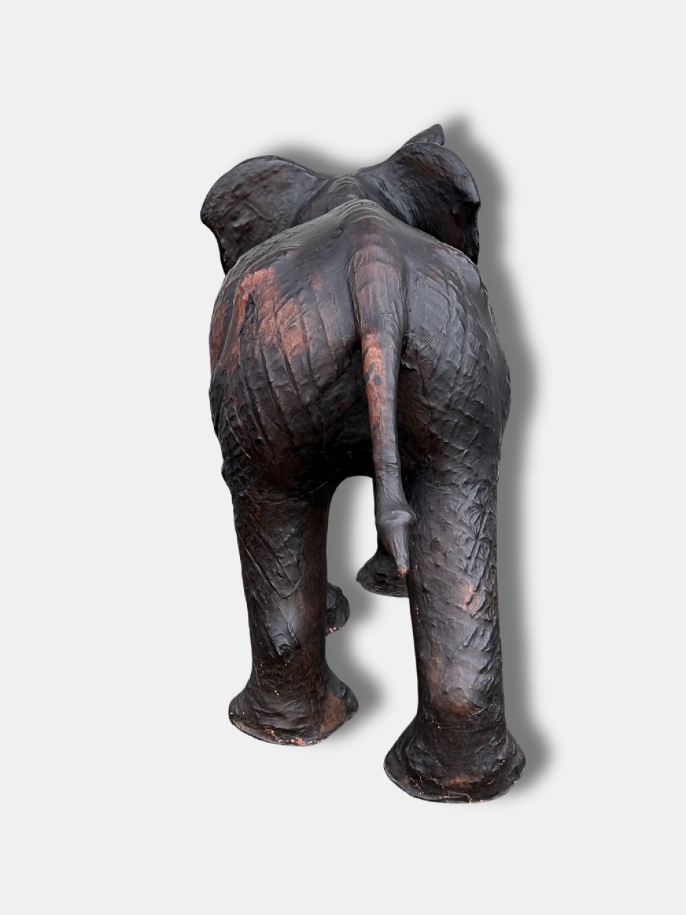 An extra-large antique dark brown leather elephant bench featuring a raised trunk, detailed hide texture, glass eyes, and short tusks. View IV