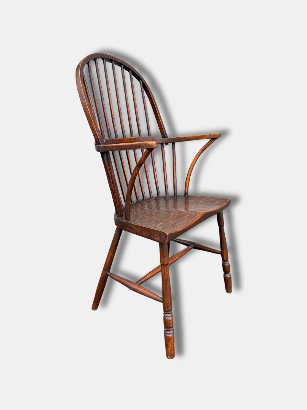 A dark timber hoop back Windsor armchair featuring vertical spindles, bentwood arm supports, a saddle seat, and turned legs with an H-stretcher.