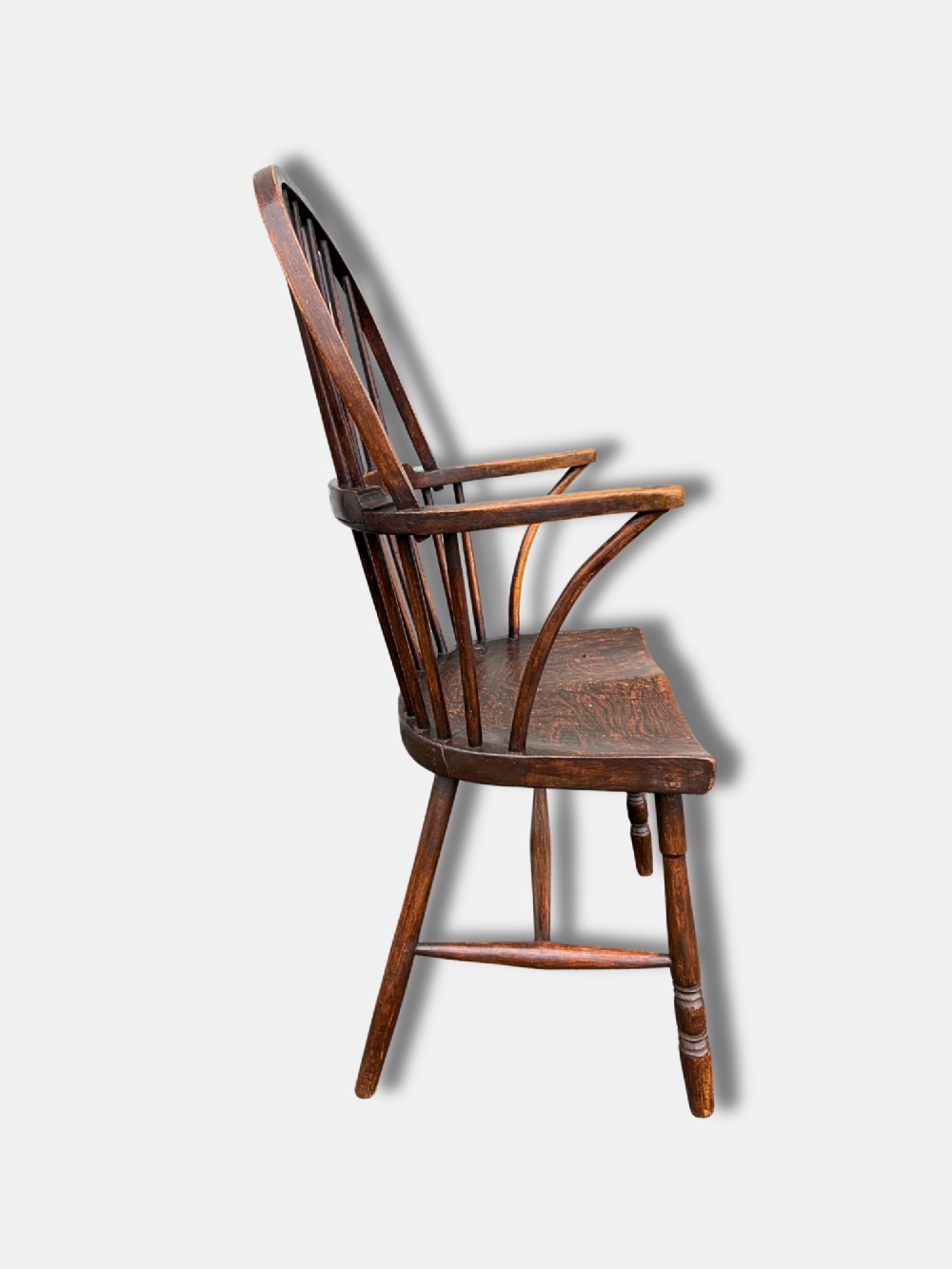 A dark timber hoop back Windsor armchair featuring vertical spindles, bentwood arm supports, a saddle seat, and turned legs with an H-stretcher. View III