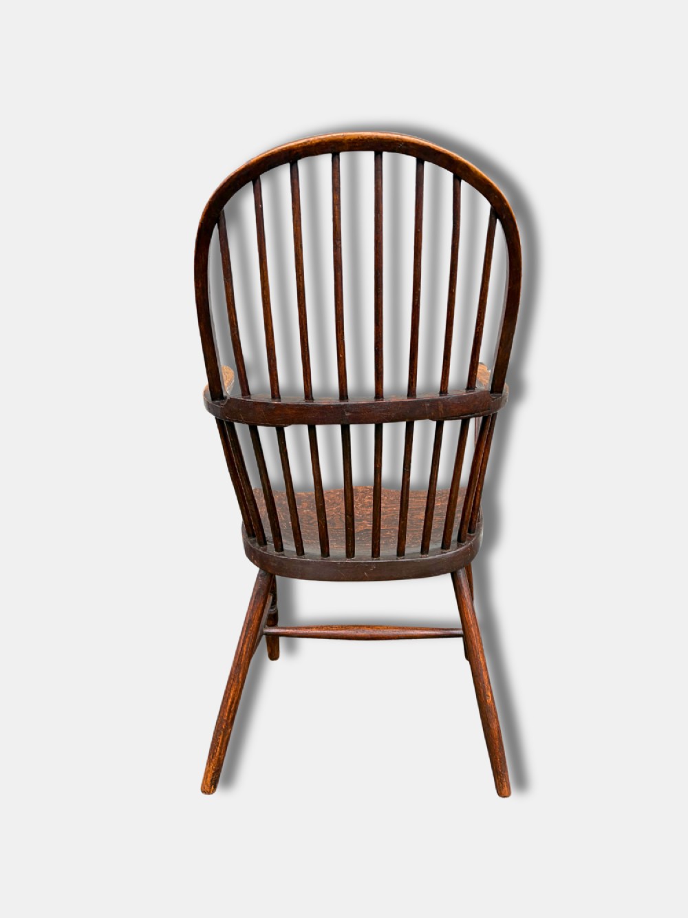 A dark timber hoop back Windsor armchair featuring vertical spindles, bentwood arm supports, a saddle seat, and turned legs with an H-stretcher. View IV