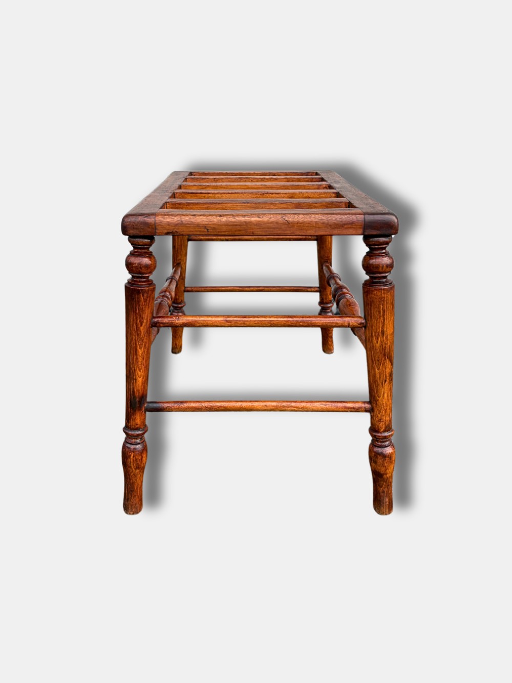 An antique c. 1900 English oak luggage stand featuring a slatted top frame and turned wooden legs with stretchers. View IV