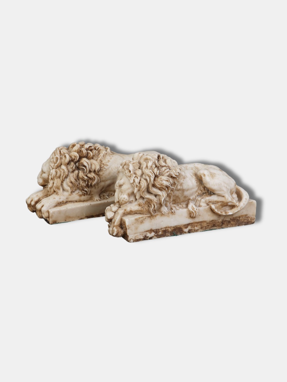 A pair of carved off-white alabaster recumbent lions resting on rectangular plinths, crafted after Antonio Canovas original designs. View II