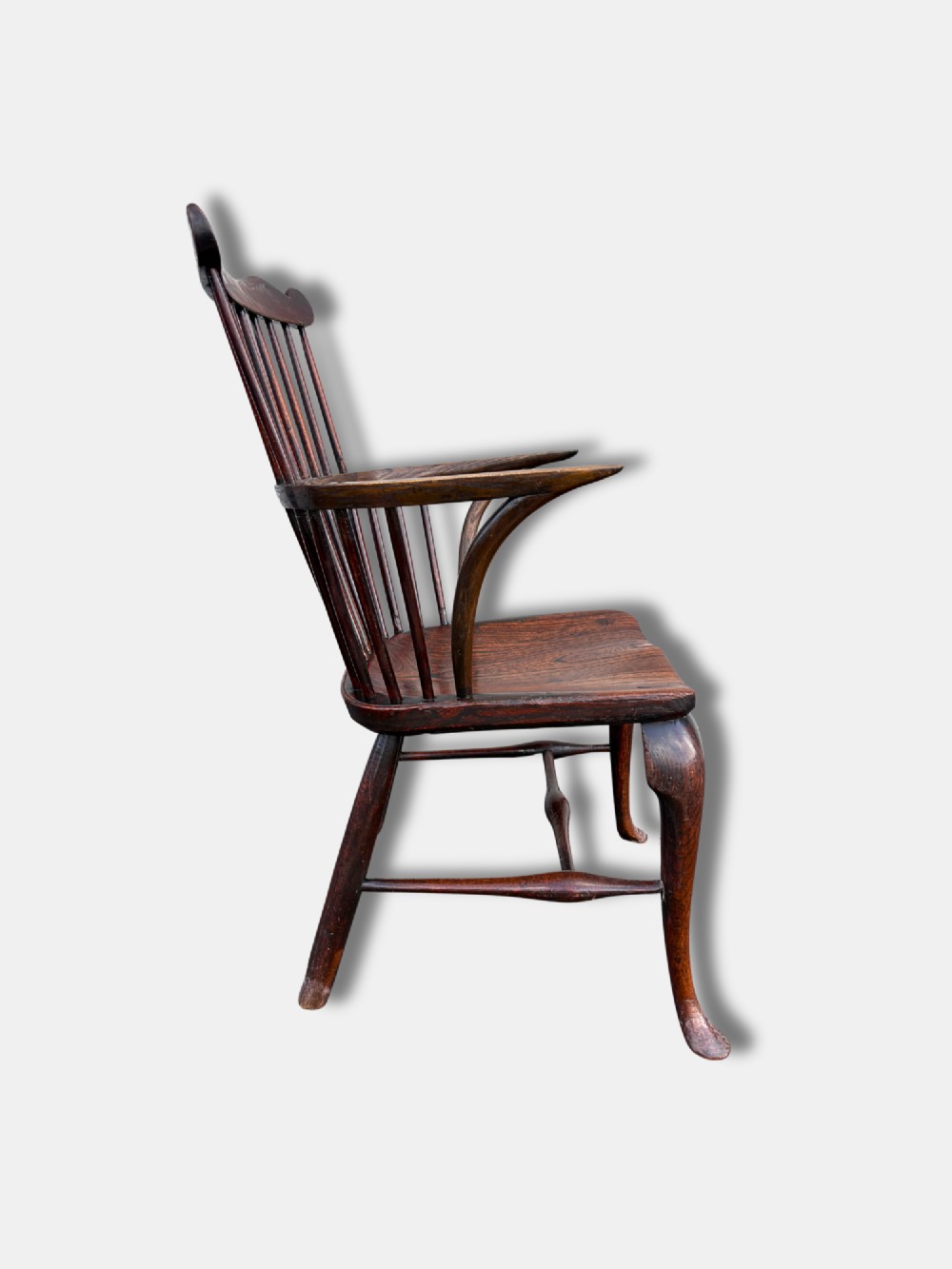 An antique dark yewwood comb back Windsor armchair featuring turned back spindles, shaped armrests, a contoured solid seat, and cabriole front legs. View III