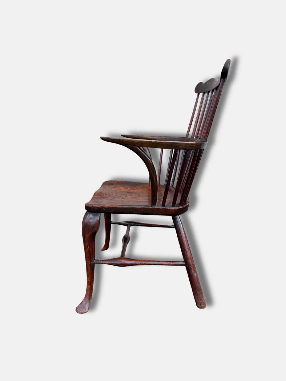 An antique dark yewwood comb back Windsor armchair featuring turned back spindles, shaped armrests, a contoured solid seat, and cabriole front legs. View IV