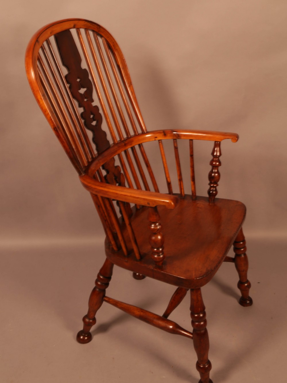 A mid-19th century high-back yew wood Windsor armchair featuring a pierced central splat, steam-bent armrests, shaped seat, and turned legs.