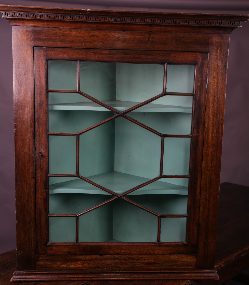 A Georgian mahogany corner cupboard featuring an astragal glazed door, dentil moulding along the cornice, and a painted green interior with three shelves.