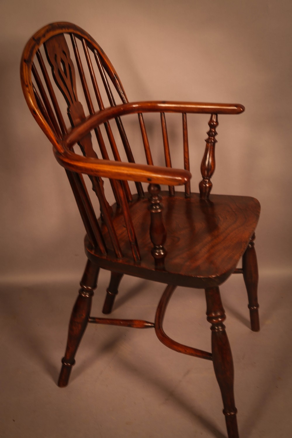 A traditional yew wood low-back Windsor armchair featuring a curved bow armrest, spindle back with central pierced splat, shaped solid seat, and turned legs with a crinoline stretcher.