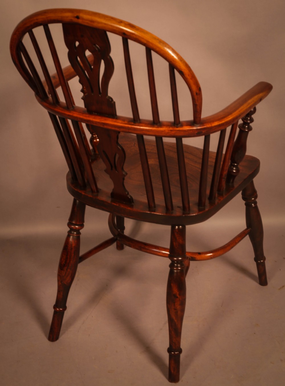 A traditional yew wood low-back Windsor armchair featuring a curved bow armrest, spindle back with central pierced splat, shaped solid seat, and turned legs with a crinoline stretcher. View V
