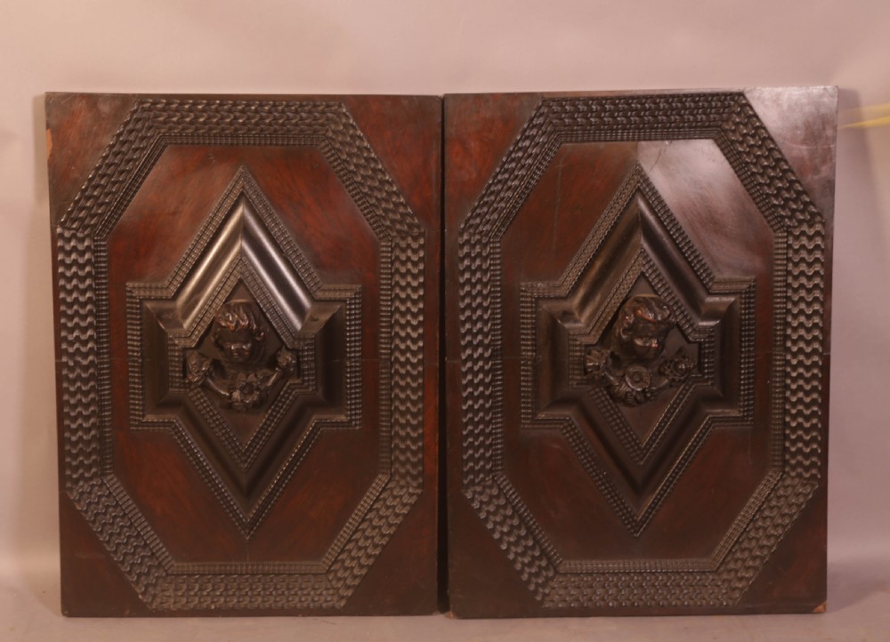 A pair of rectangular dark oak door panels featuring central raised diamond motifs carved with human heads and intricate geometric chip-carving borders.