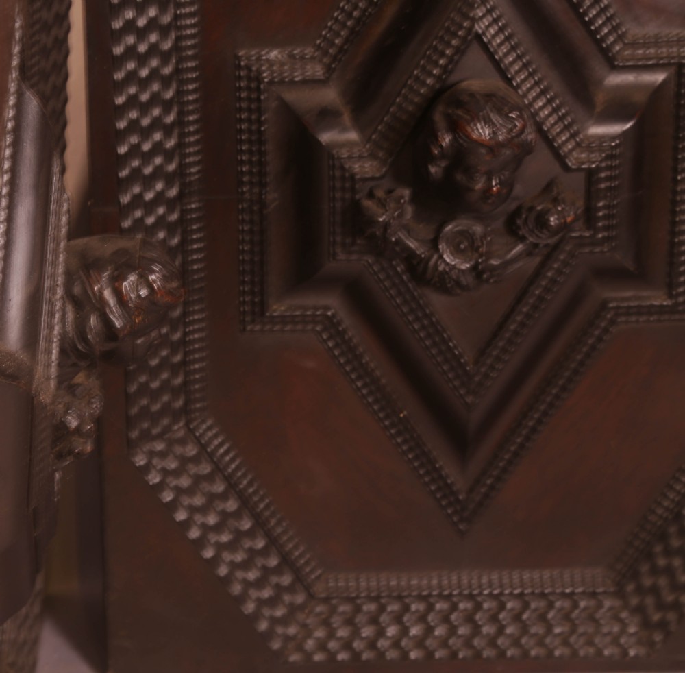 A pair of rectangular dark oak door panels featuring central raised diamond motifs carved with human heads and intricate geometric chip-carving borders. View V