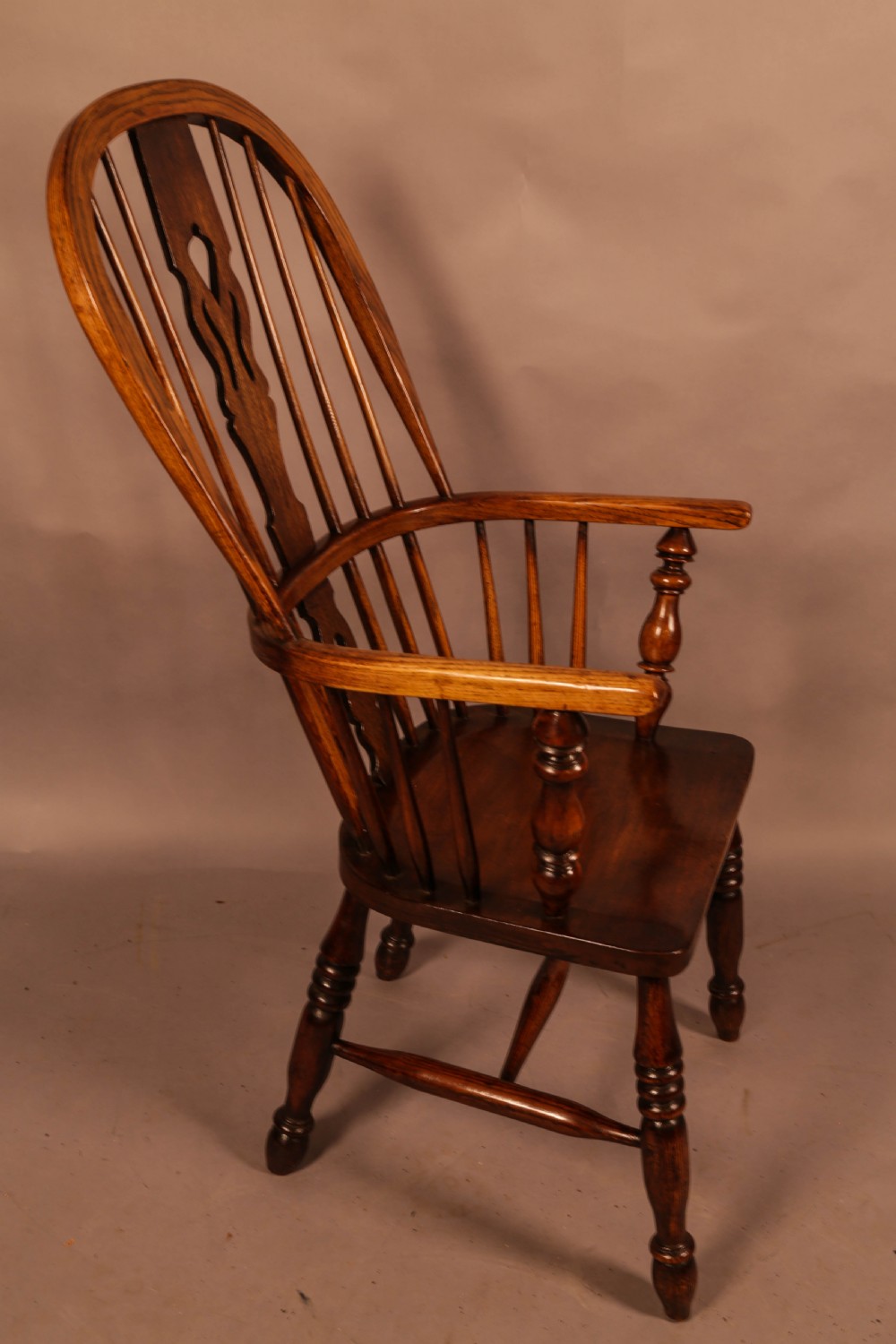 An antique high-back Windsor armchair crafted from ash and elm timber with turned legs and a pierced back splat.