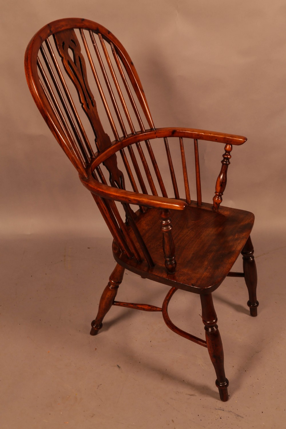 A high-backed wooden Windsor armchair featuring a pierced splat, slender spindles, and turned legs joined by an H-stretcher.