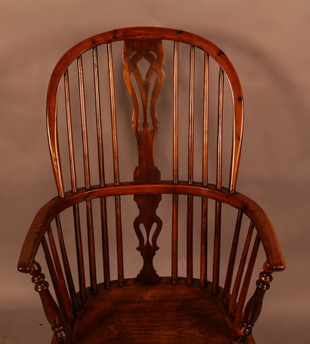 A high-backed wooden Windsor armchair featuring a pierced splat, slender spindles, and turned legs joined by an H-stretcher. View V