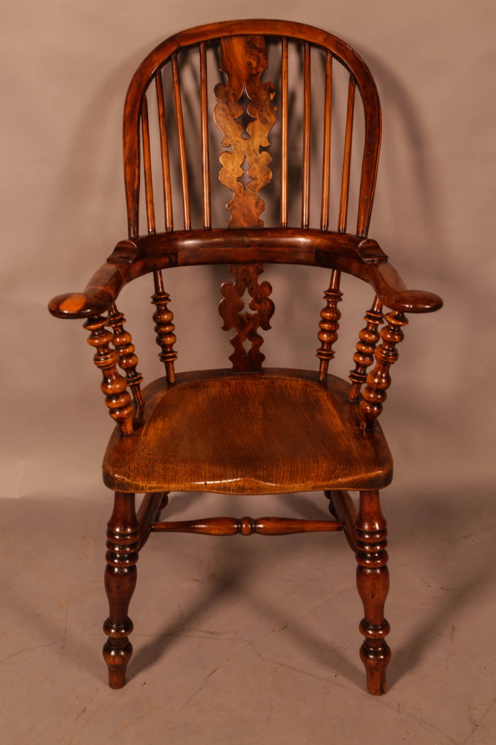 An antique brown yew wood Windsor armchair featuring a hoop back, a central pierced splat, turned spindles, broad armrests, and turned legs. View II