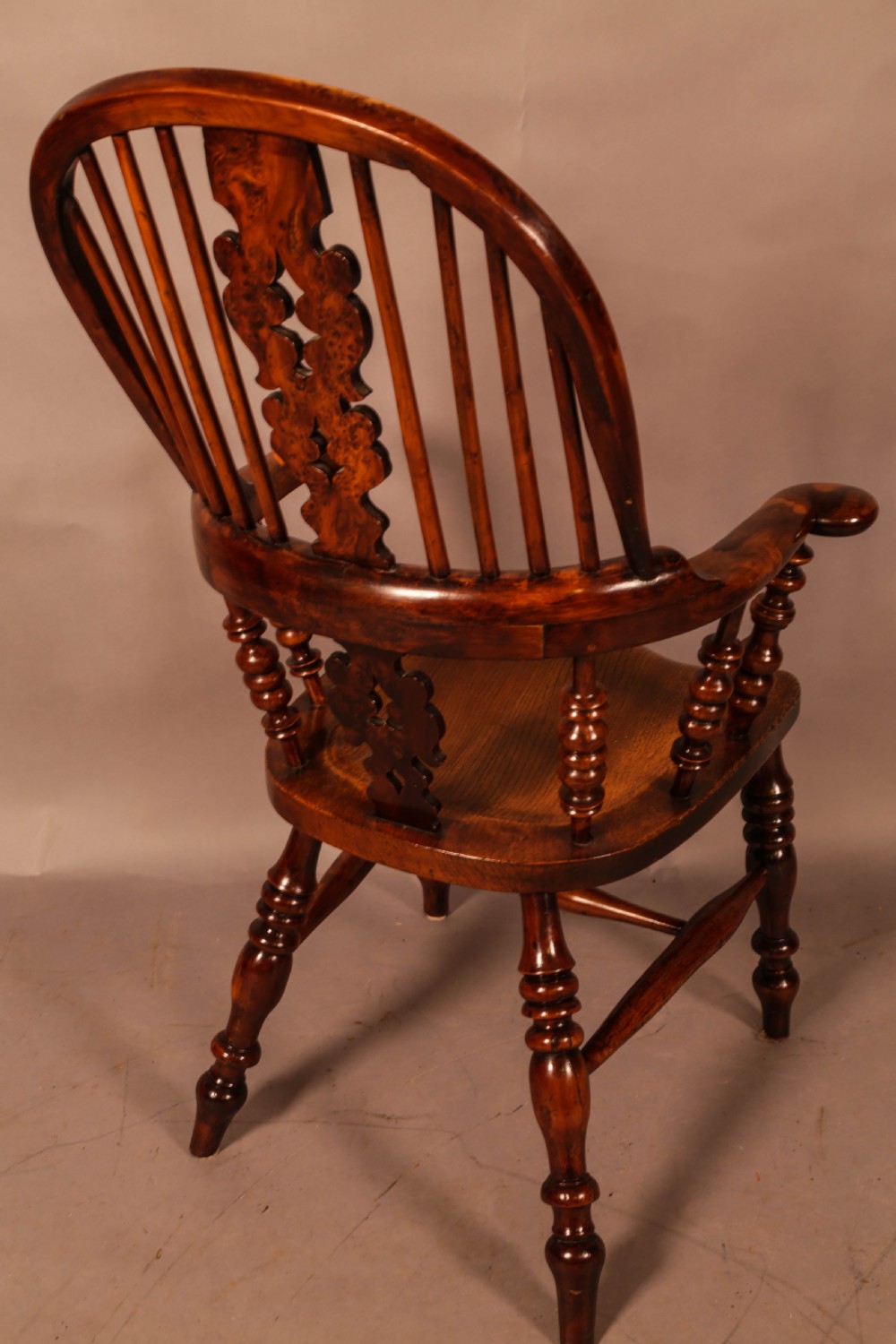 An antique brown yew wood Windsor armchair featuring a hoop back, a central pierced splat, turned spindles, broad armrests, and turned legs. View III